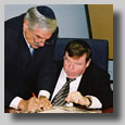 The men around the round table doin' bizness. Harvey marks signing away.